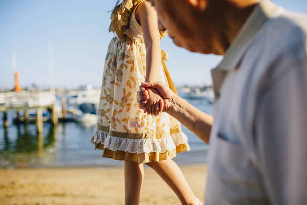 A touching scene of a grandfather holding his granddaughter's hand by the seaside on a sunny day.