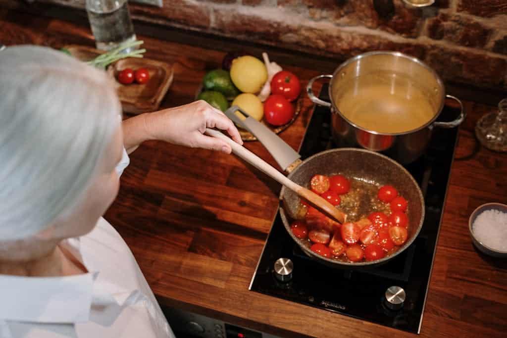 A senior woman prepares a homemade tomato sauce in a warm, cozy kitchen setting.