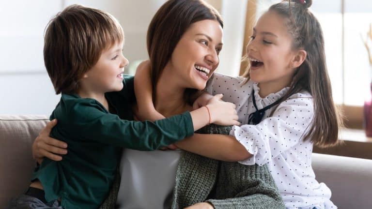 Mama i njezine dvije djevojčice u zagrljaju, nasmijane i sretne.